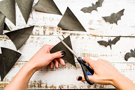 female hands with black nails cutting halloween flags on white wooden table top view
