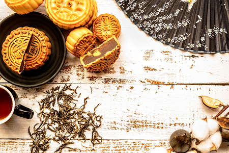 traditional chinese mid autumn festival food mooncakes on white wooden background with tea, leaves and flowers top view flat layの写真素材