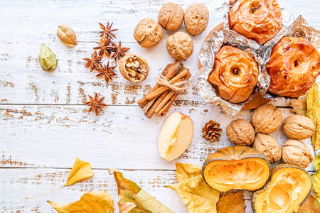 thanksgiving day concept. backed apples in foil with walnuts and cinnamon on white wooden background top view flat layの写真素材