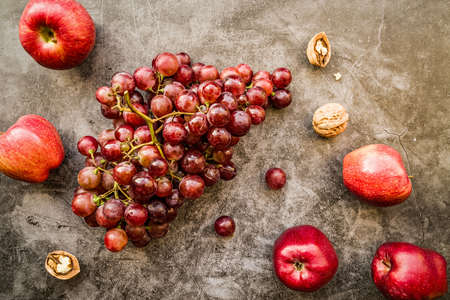 raw purple and red fruit: grapes, apples and walnuts top view on dark background flat lay. Healthy...
