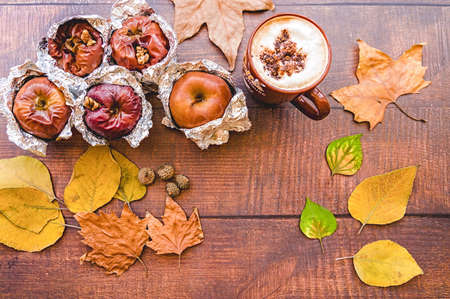 backed apples in foil with cup of coffee and autumn leaves on wooden backgroundの写真素材