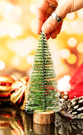 christmas and new year concept. hand holding small christmas tree surrounded with decorations on bright blurry shiny backgroundの写真素材
