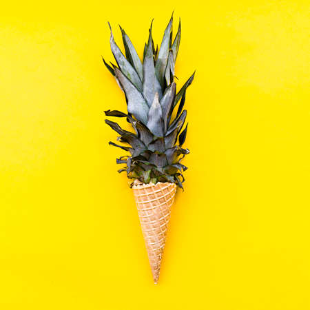 Ice cream cone with pineapple leaves on bright yellow background flat lay top viewの写真素材