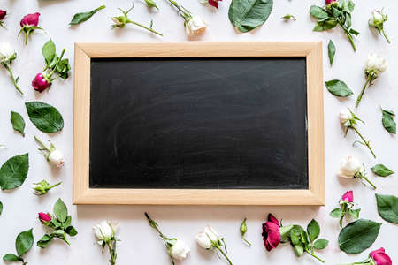 Scattered rose flowers around black chalkboard with copyspaceon light marble background flat lay top viewの写真素材