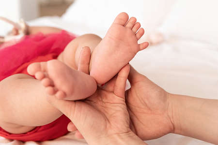 mother hands holding baby feet on the white bed