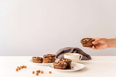 chocolate cupcakes with glazing, walnuts and a cup of coffee on white table front viewの写真素材