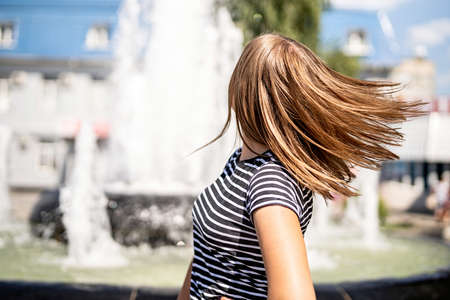 True happiness concept. Young caucasian woman in casual clothes shaking her hair on urban fountain backgroundの写真素材