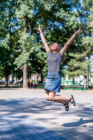 True happiness concept. Happy laughing caucasian woman in casual clothes jumping raising her hands to the sky in the park in summer dayの写真素材