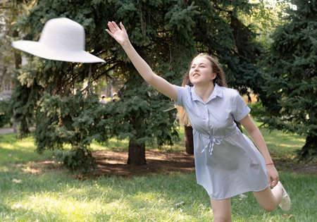 True happiness concept. Young caucasian blond woman in a blue stripped summer dress throwing her hat...