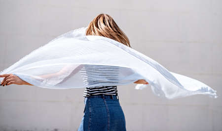 young woman with a blue fabric turning around on grey background