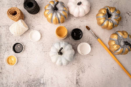 Halloween concept. Halloween DIY crafts. White and gold painted pumpkin on the table with pains top...
