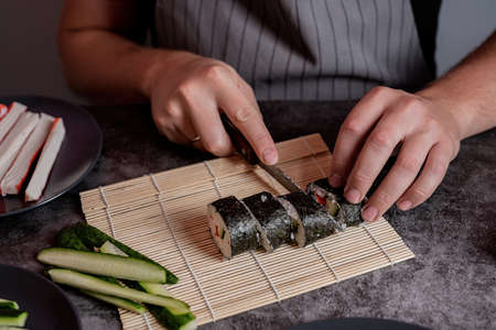 Man in a grey apron cutting homemade sushi roolsの写真素材