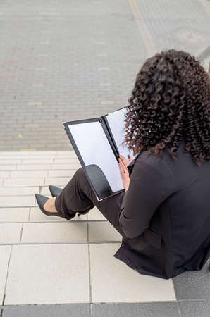 outdoor portrait of a business woman sitting on the stairs looking at the documents