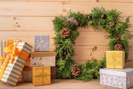 Christmas concept. Christmas wreath decorated with pine cones, chestnuts and a pile of gift boxes on wooden backgroundの写真素材