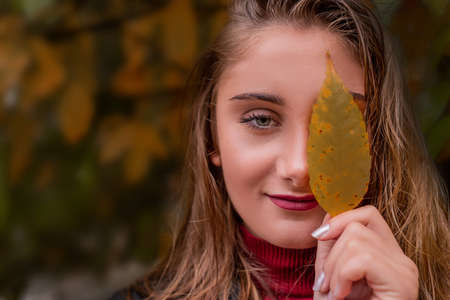Autumn seasonal concept. Beautiful woman holding a yellow leaf in front of her face