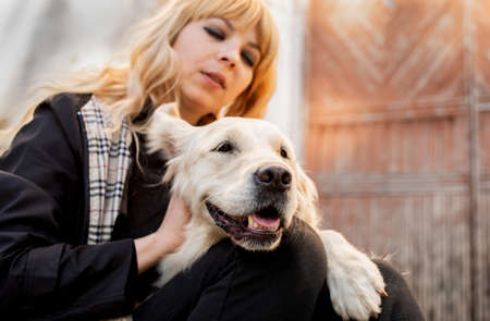 Pet care concept. Blond caucasian woman hugging her golden retriever dog outdoorsの写真素材