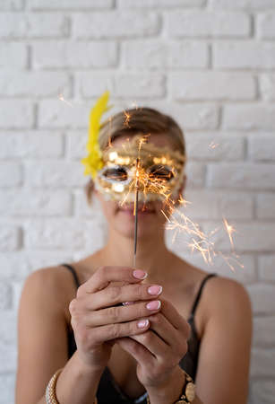 Woman in a party dress and a mask holding a sparkler in her hands