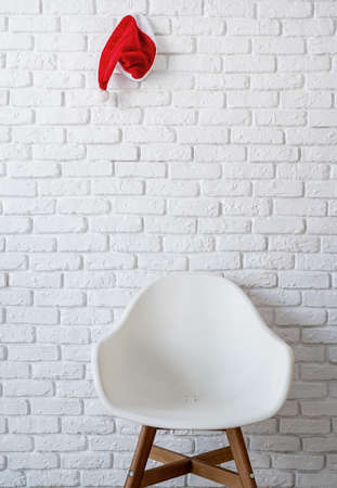 Minimal interior with a chair and a red santa hat hanging on the white brick wallの写真素材