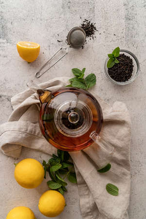 Hot black tea in a teapot decorated with mint leaves, lemons and dry tea leaves flat lay top viewの写真素材