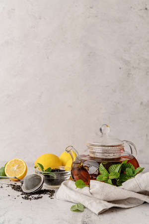 Hot black tea in a teapot decorated with mint leaces, lemons and dry tea leaves front view with copy spaceの写真素材