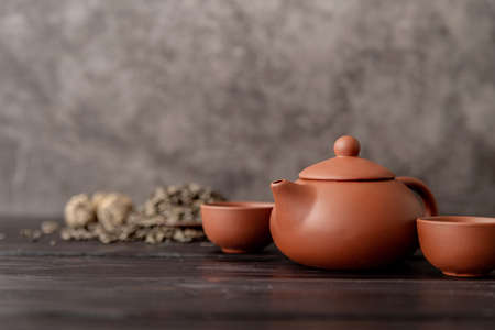 Brown chinese tea set with green tea leaves on dark wooden table front view with copy space