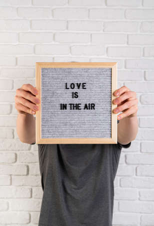 Valentines day concept. Man hands holding a black felt letter board with the words Love Is In The...