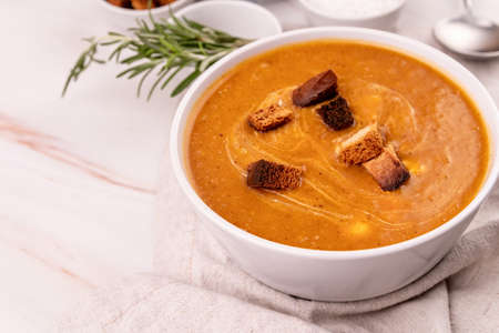 Pumpkin soup with croutons in white bowl decorated with a tablecloth, rosemary and spicesの写真素材
