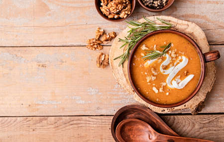 Pumpkin soup with creme in brown bowl decorated with walnuts top view flat lay with copy space on wooden backgroundの写真素材