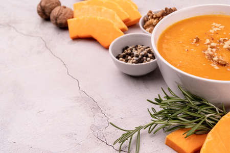 Pumpkin soup with walnuts in white bowl decorated with pumpkin slices and spices top view flat lay with copy spaceの写真素材