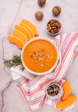 Pumpkin soup with walnuts in white bowl decorated with pumpkin slices and spices top view flat layの写真素材
