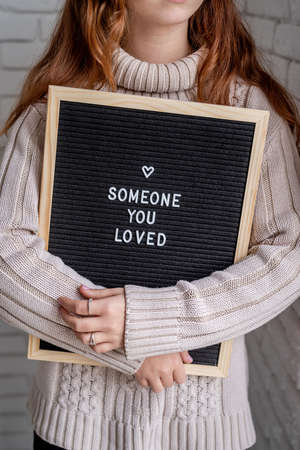 Valentines Day concept. Sad beautiful woman holding felt letter board with the words Someone You Lovedの写真素材