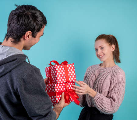Pretty young smiling woman accepting gifts from her boyfriend isolated on blue background