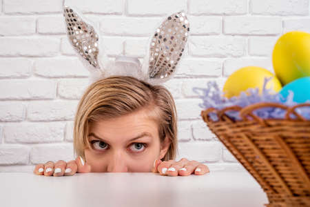 Easter holiday concept. Blond woman with bunny ears looking at the basket with Easter colored eggs...