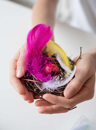 Easter holliday concept. CChild hands holding a nest with a colorful quail egg and feathersの写真素材