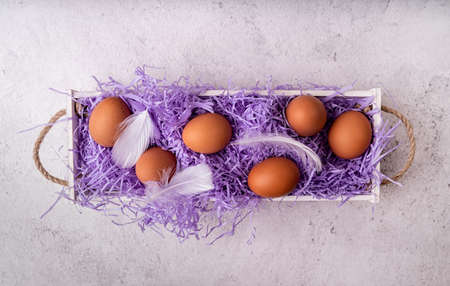 Easter holiday concept. White wooden box with chicken eggs on white marble background top view flat...