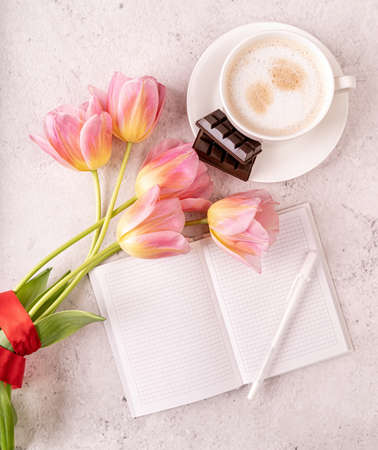 Cup of cappuccino, notebook and pink tulips top view on marble background