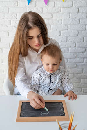 Mother teaching her little son to draw on the chalkboardの写真素材