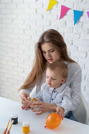 Mother teaching her little son to paint opening a container with gold paintの写真素材