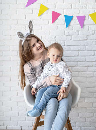Woman in bunny ears hugging her little son at home on white brick wall backgroundの写真素材