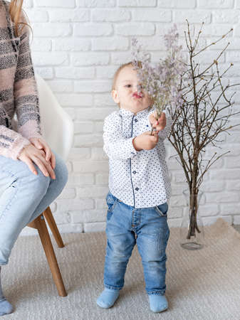 Small child giving flowers to his mom at home on white brick wall background