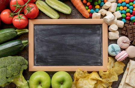 Healthy and unhealthy food concept. Fruit and vegetables vs sweets and potato fries around the blank chalk board top view flat layの写真素材