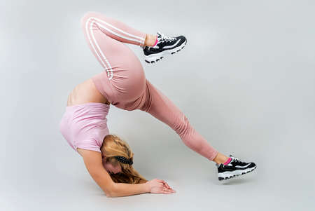 Fitness, sport, training and lifestyle concept. Acrobat woman wearing pink sportswear working out in the studio isolated on gray background with copy spaceの写真素材