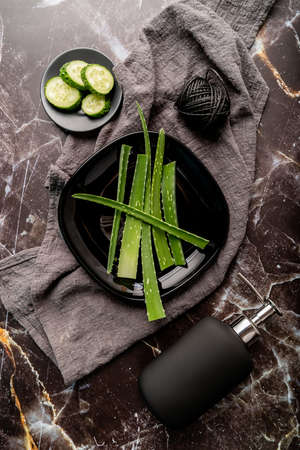 Body treatment. Top view of natural cosmetics with aloe vera, cucumbers and gel dispenser on dark marble backgroundの写真素材