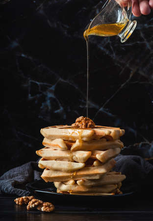 Homemade belgian waffles poured with honey front view on dark background