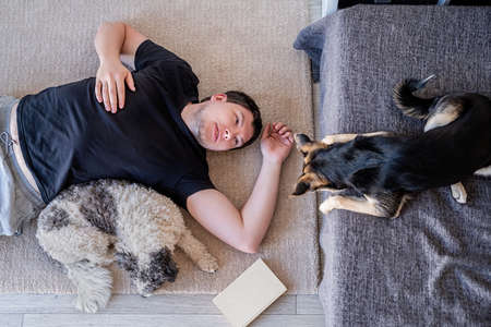 Young man lying on the floor at home with his dogsの写真素材