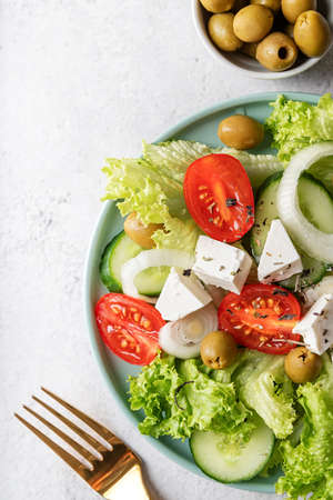 Healthy food. Top view of greek salad with olives, feta cheese and fresh vegetables on blue plate with golden forkの写真素材