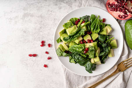 Healthy food concept. Fresh salad with avocado, spinach and pomegranate top view on white background with copy spaceの写真素材