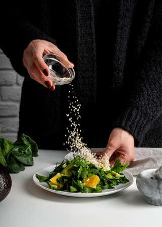 Step by step preparation of spinach, avocado and orange salad. Step 8 - pouring sesame seeds for decoration, front view, selective focusの写真素材