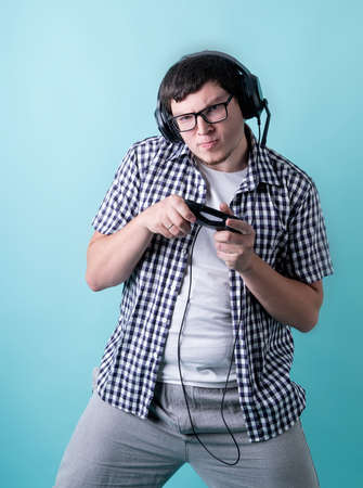 Funny young man playing video games holding a joystick isolated on blue background