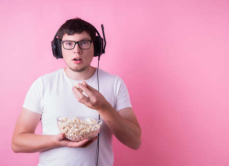 Young funny man watching a movie eating popcorn isolated on pink backgroundの写真素材